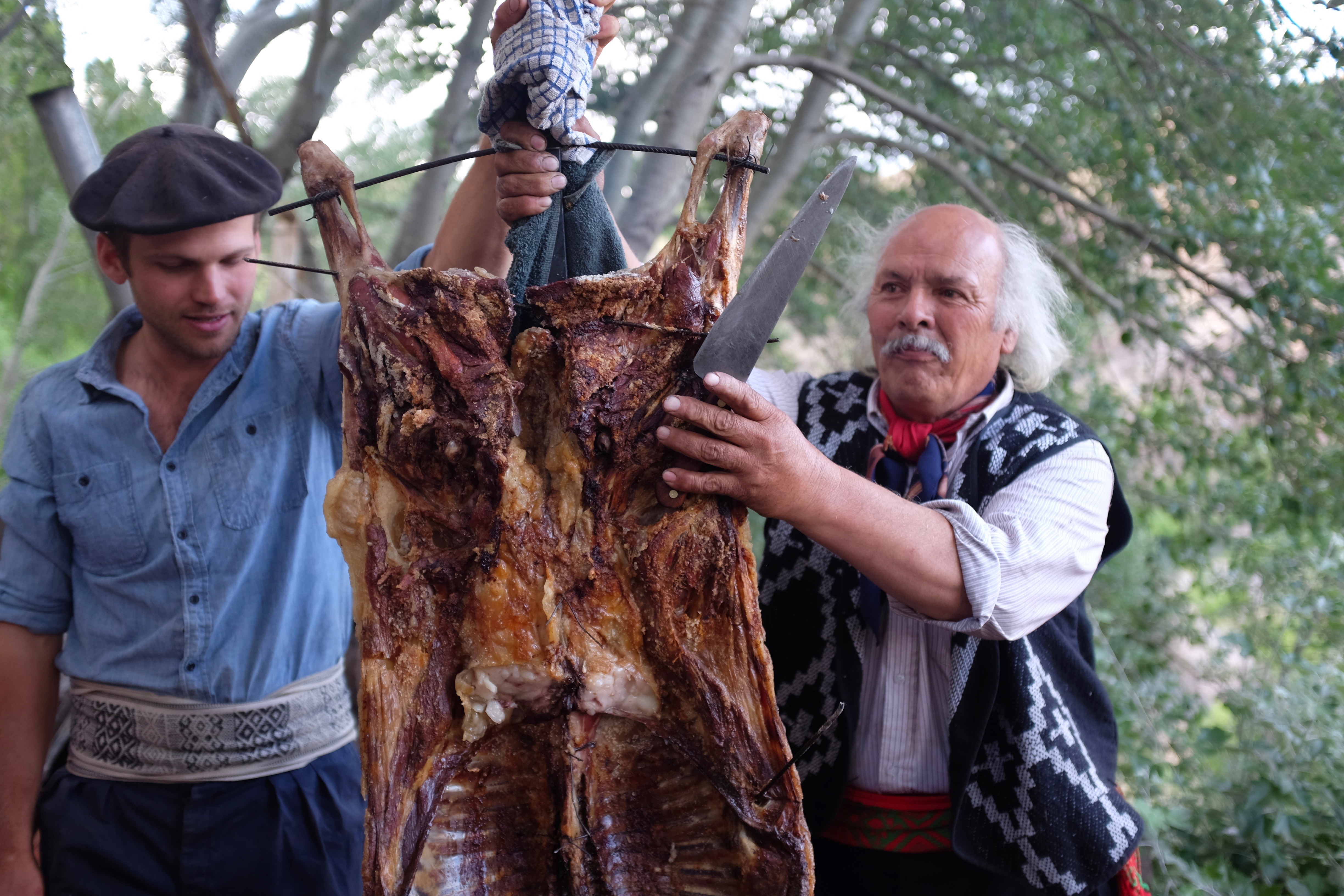 Gaucho and friend carving a roast goat at a traditional Argentine asado at Estancia Ranquilco