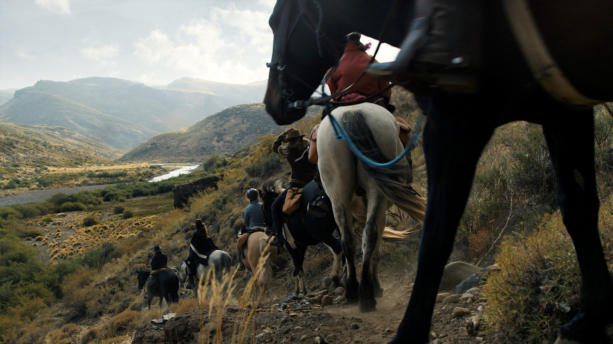 String of riders descending into a river valley in the backcountry of Estancia Ranquilco