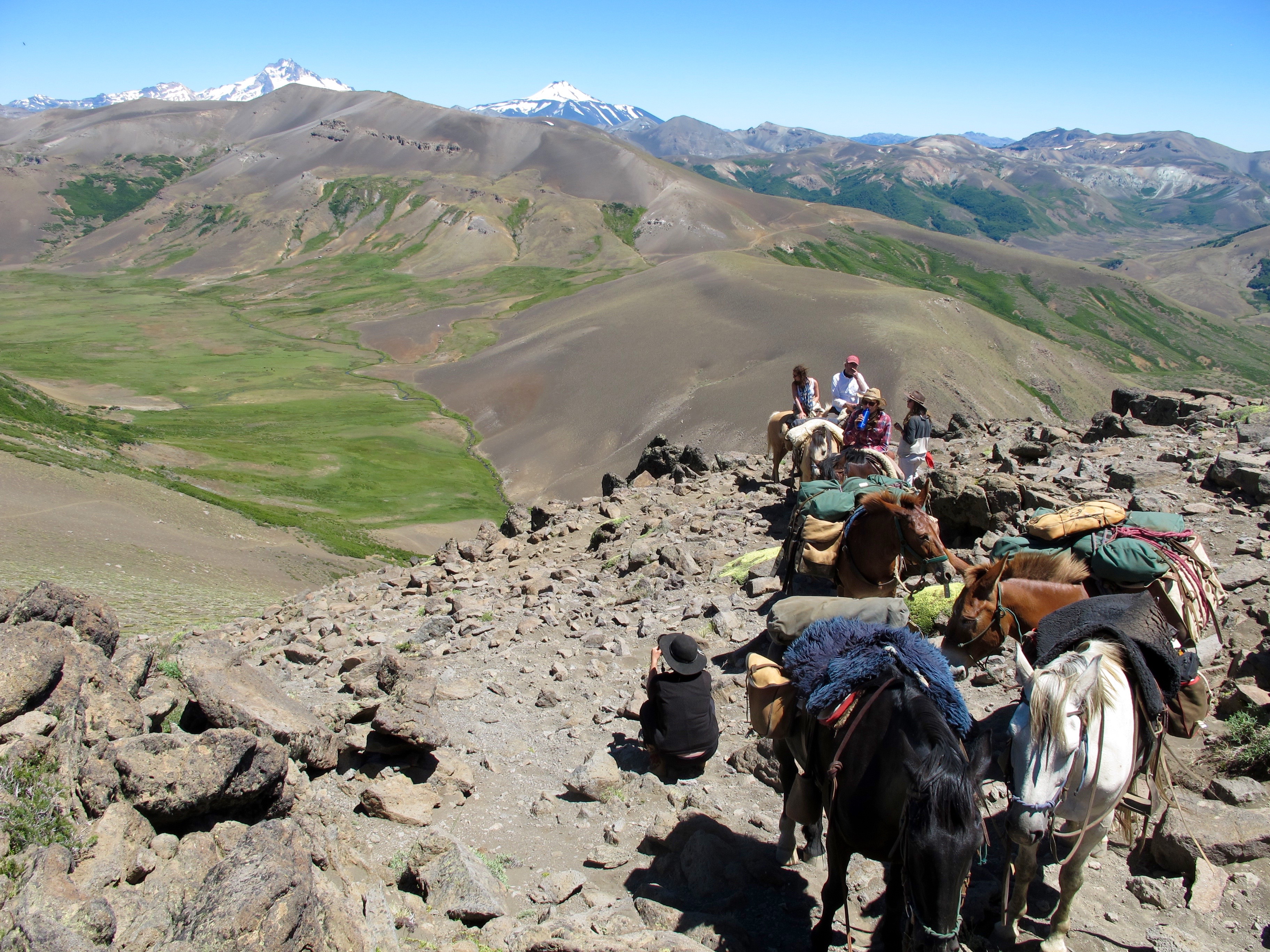 People and horses looking out over view of mountains with active volcano in background during horse pack trip at Estancia Ranquilco