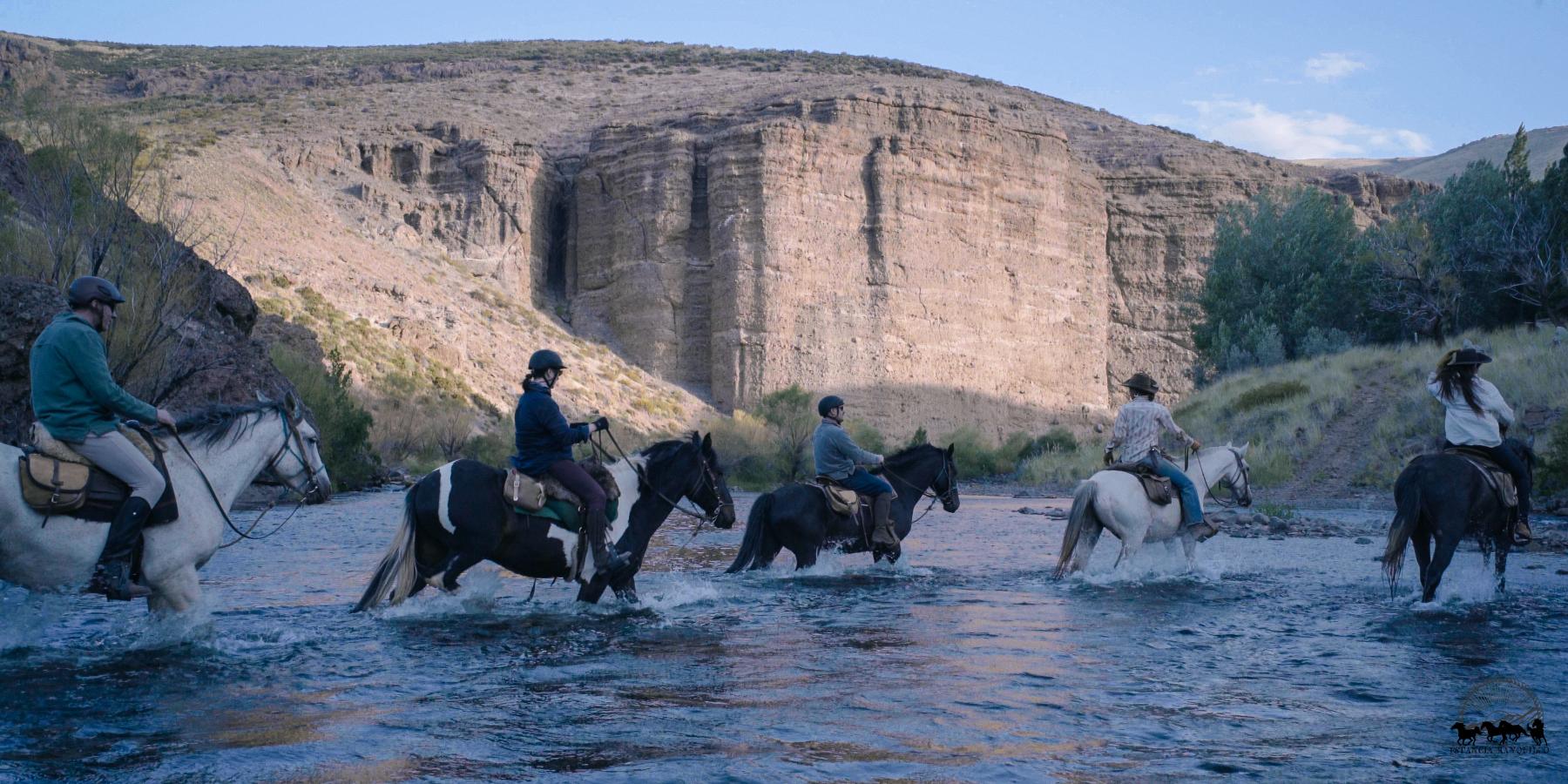 Riders on horseback crossing the river on the approach to Estancia Ranquilco in Patagonia Argentina