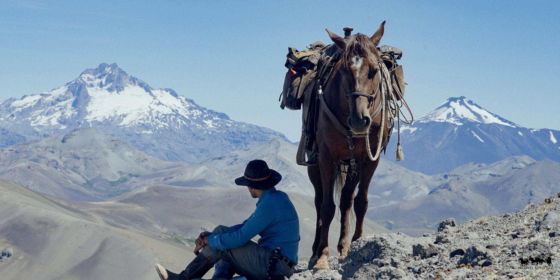 Man sitting next to horse overlooking snow capped mountains in Patagonia