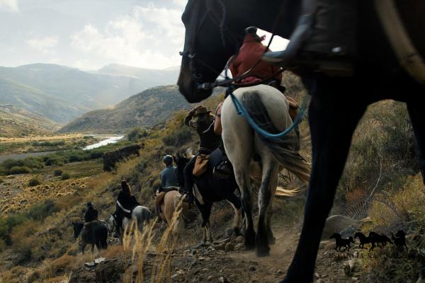 String of riders descending into a river valley in the backcountry of Estancia Ranquilco